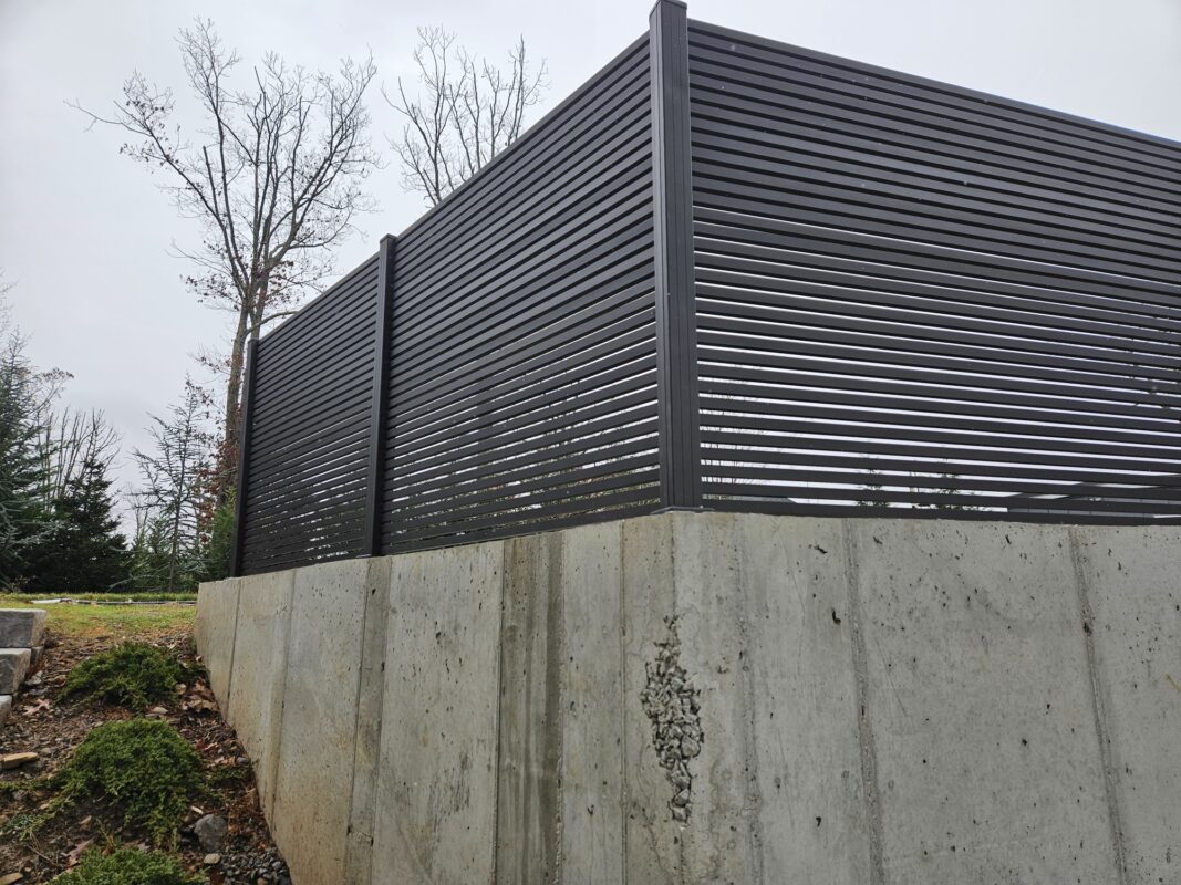Corner section of black aluminum wall topper above a concrete wall