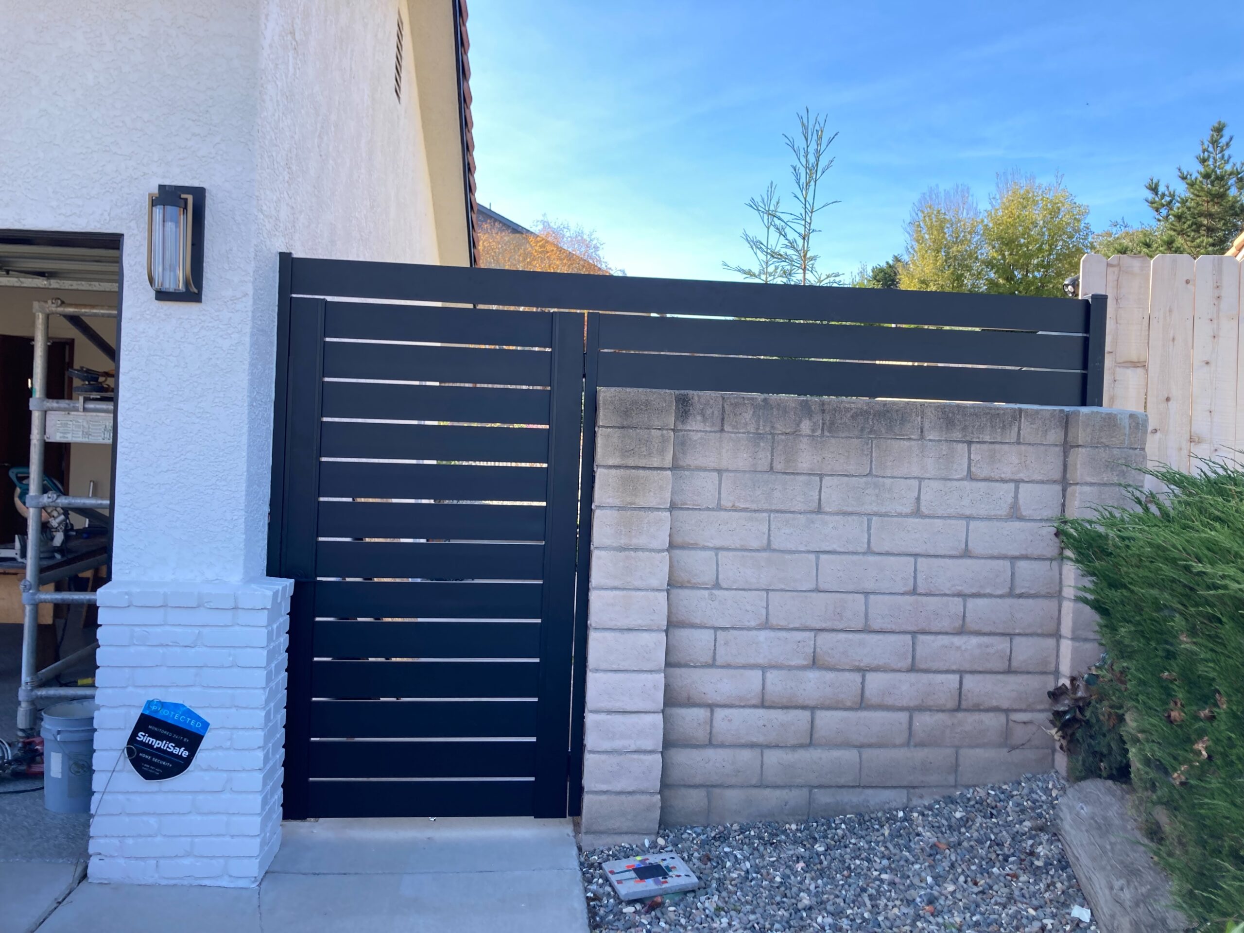 Front View of a Black Pedestrian Gate and Wall Topper Installed On Side of a House