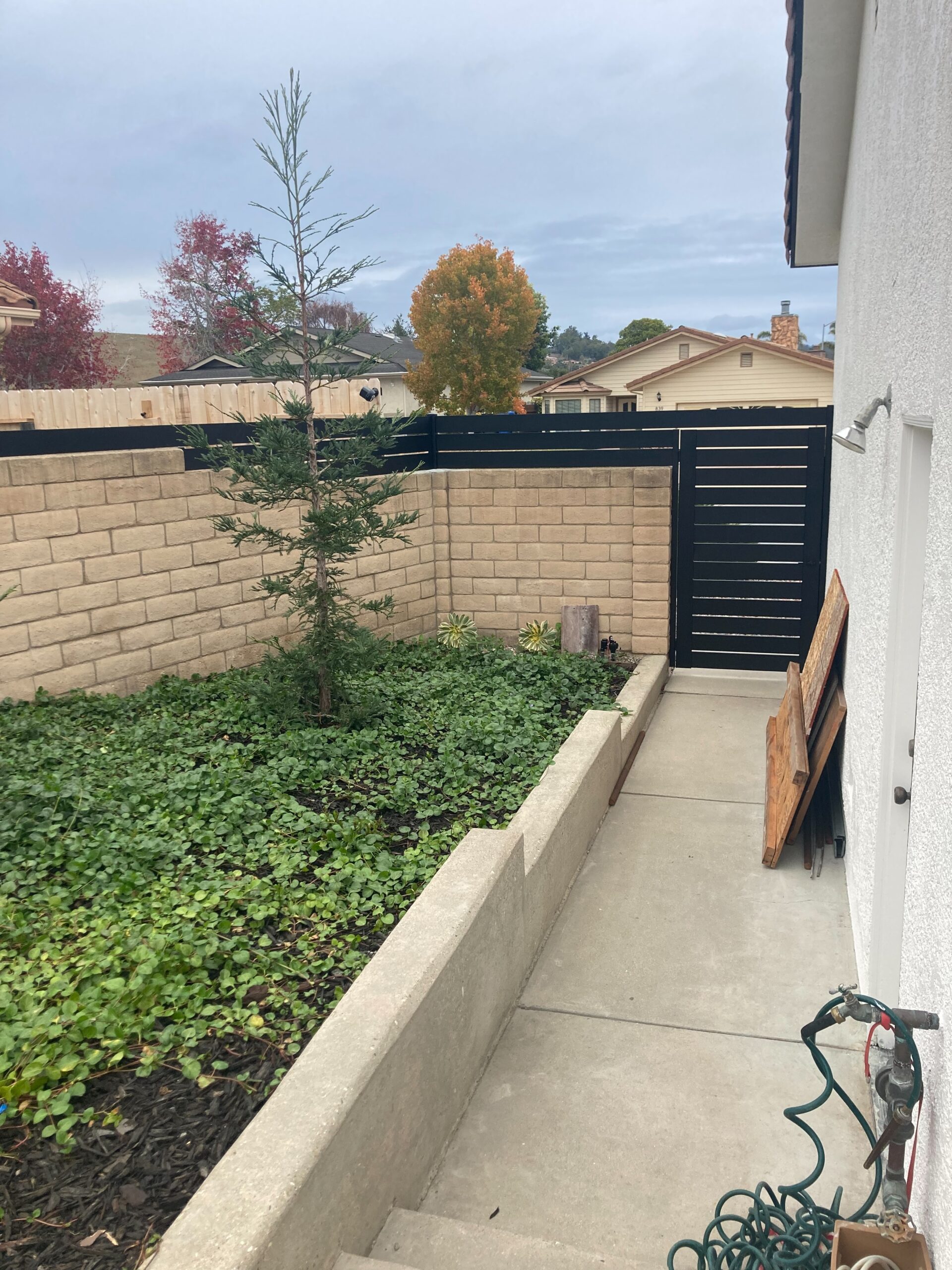 Back View of a Black Pedestrian Gate and Wall Topper Installed On Side of a House