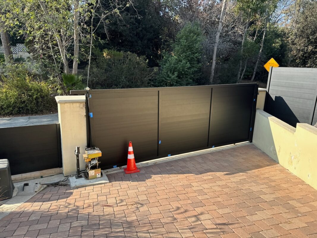 Modern black sliding driveway gate installation with a brick driveway.