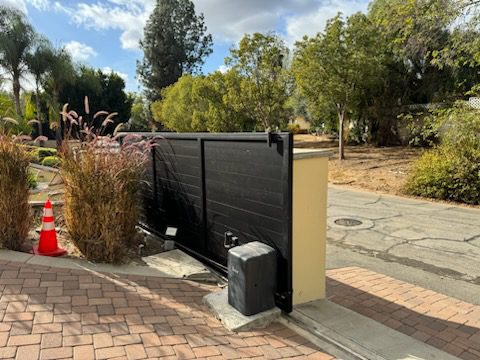 Modern black sliding driveway gate with surrounding foliage and brick pavers in Whittier.
