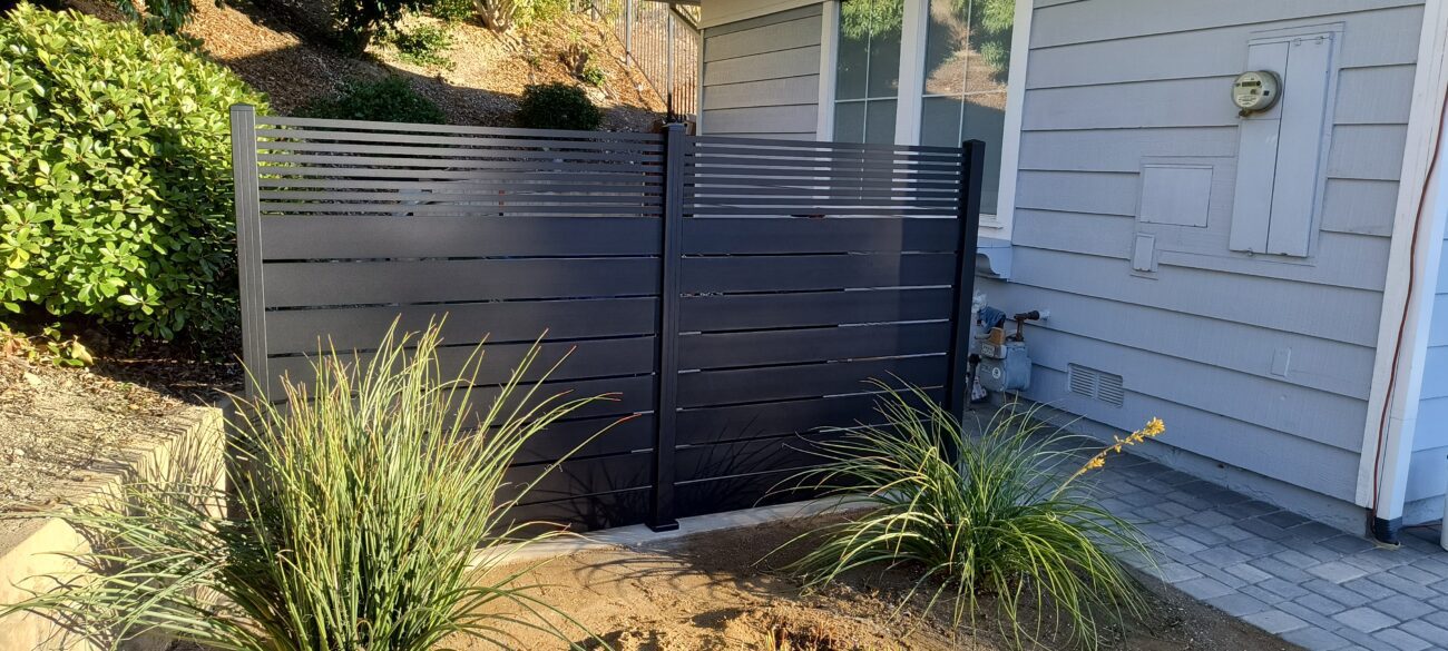 A modern black aluminum gate is installed next to a house, enhancing security and style.