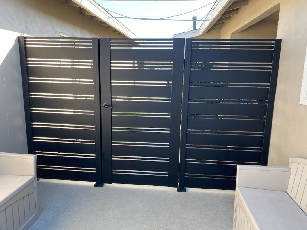 Black aluminum pedestrian gate with sleek slats in a residential side yard.