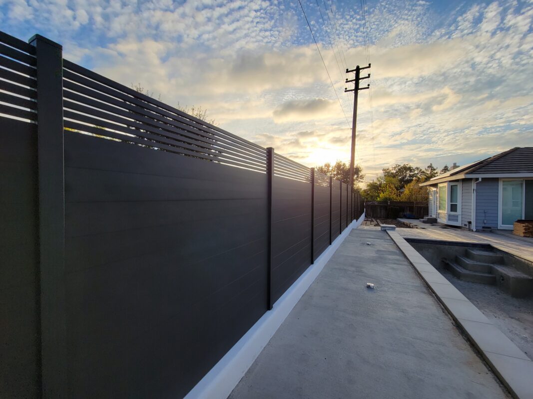 Black aluminum fence panels installed alongside a residential property under a sunny sky.