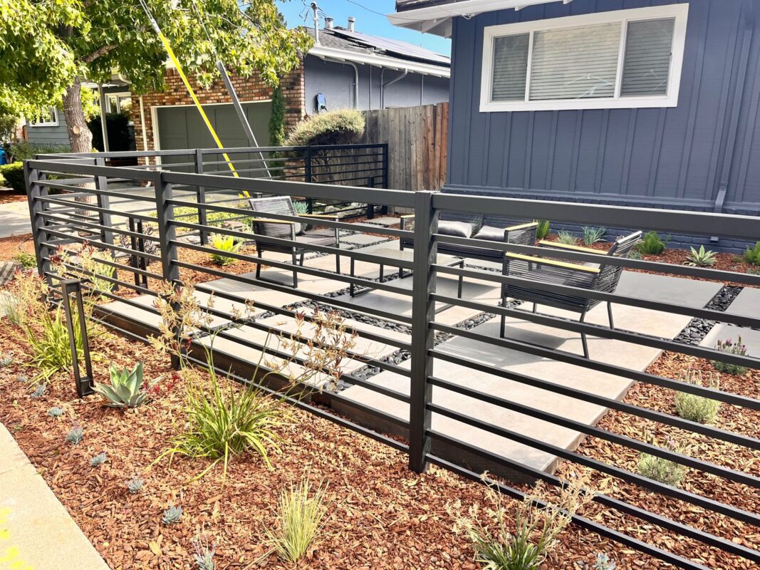 Modern black fence with top rail secures a landscaped outdoor seating area.