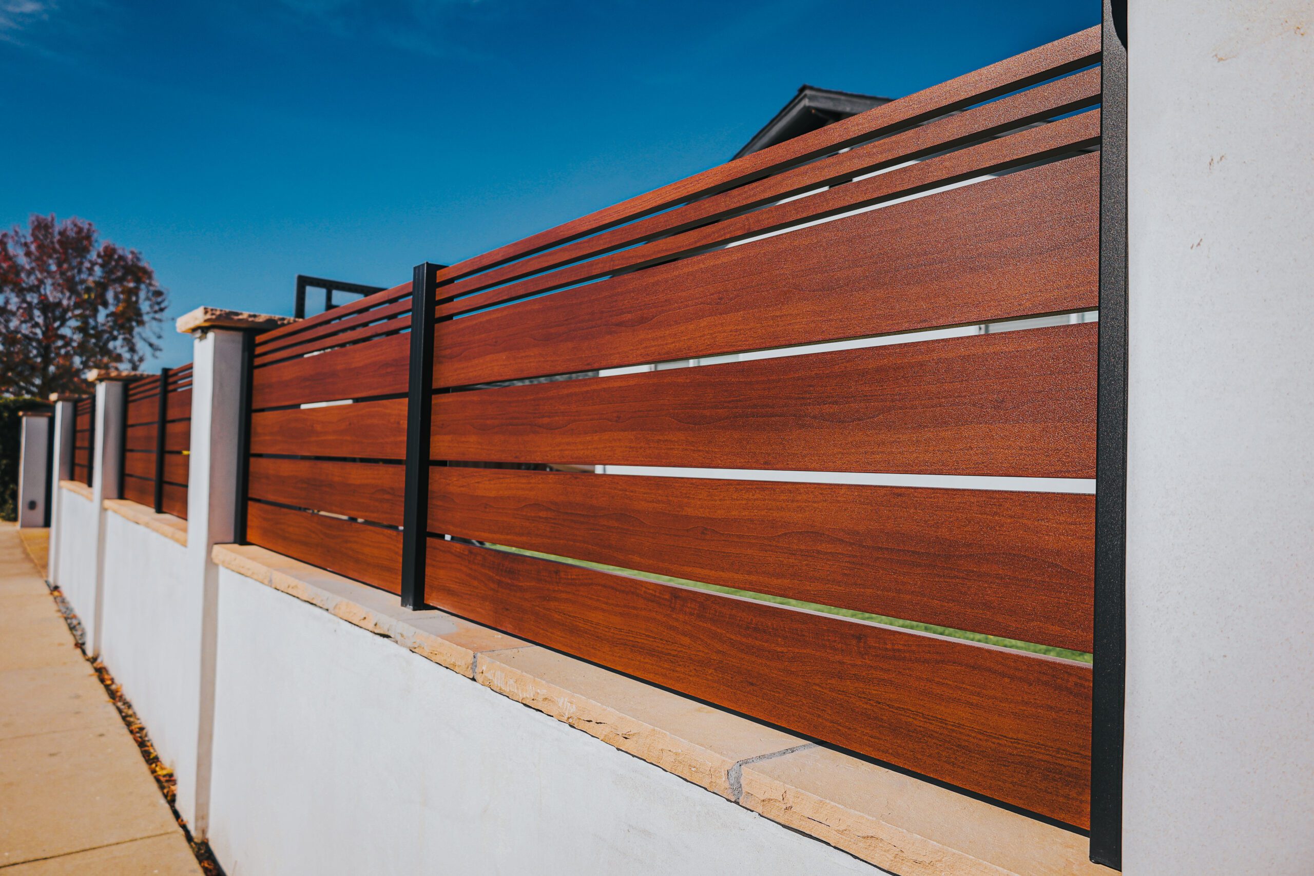 Close-up of modern aluminum fence with wood-like finish against a blue sky backdrop.