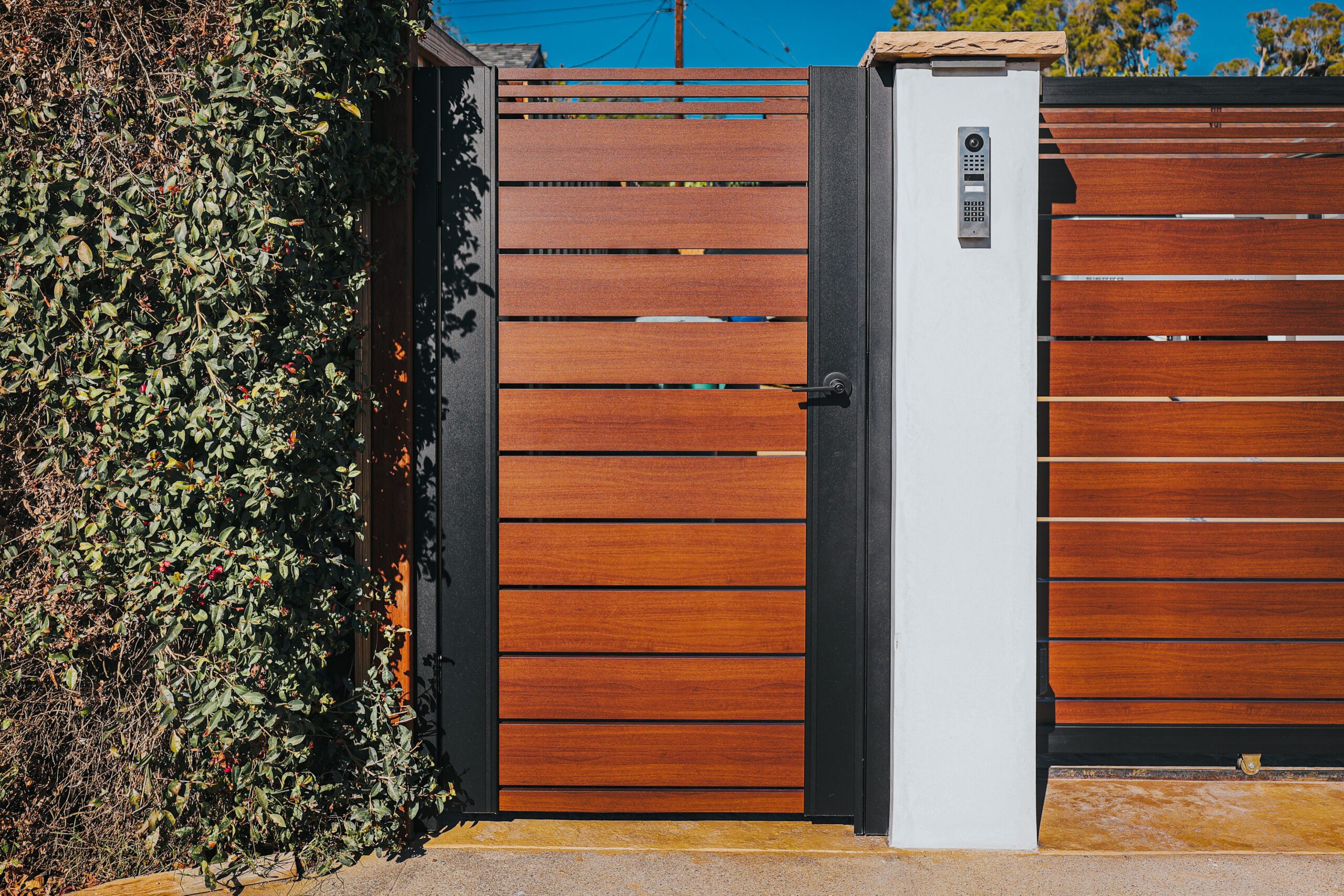 Modern aluminum gate with wood-like appearance, surrounded by lush greenery.
