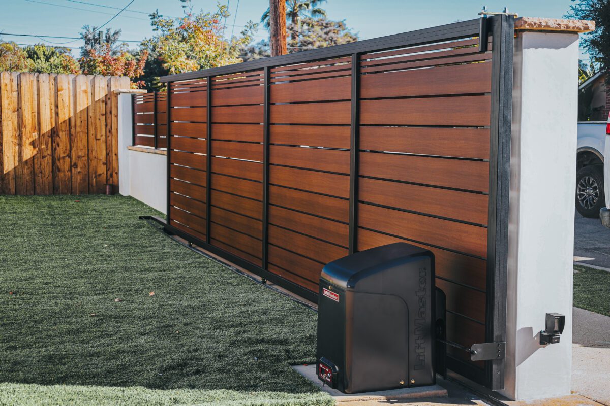 A newly installed aluminum fence with a wood-like finish and automated gate opening mechanism.