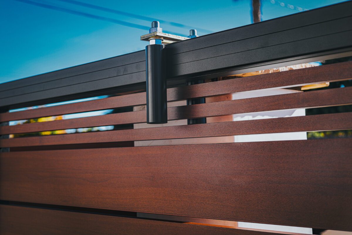 Close-up of a modern aluminum fence with wood-like finish under blue sky.