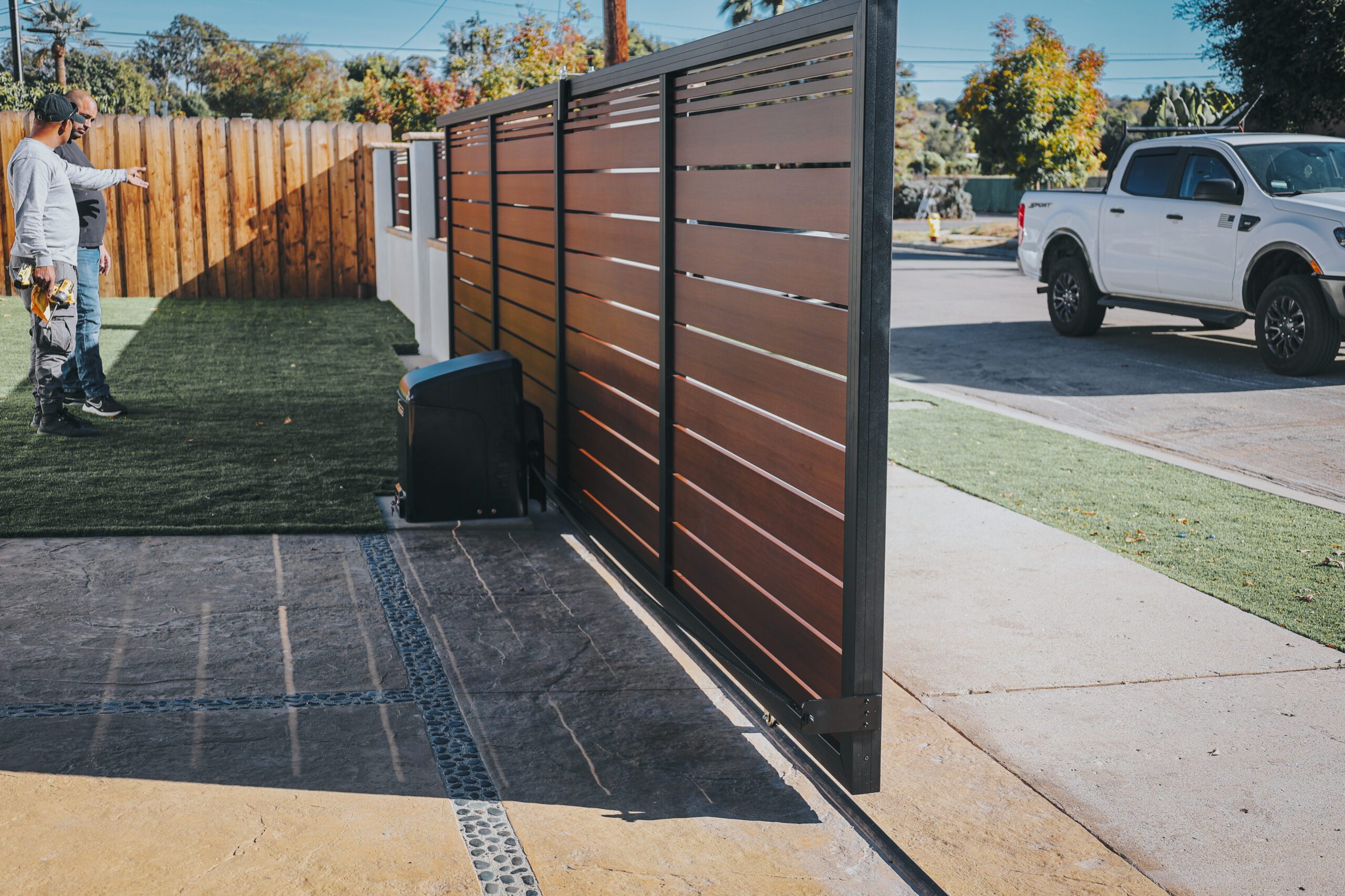 Men discussing a modern aluminum gate installation beside a driveway.