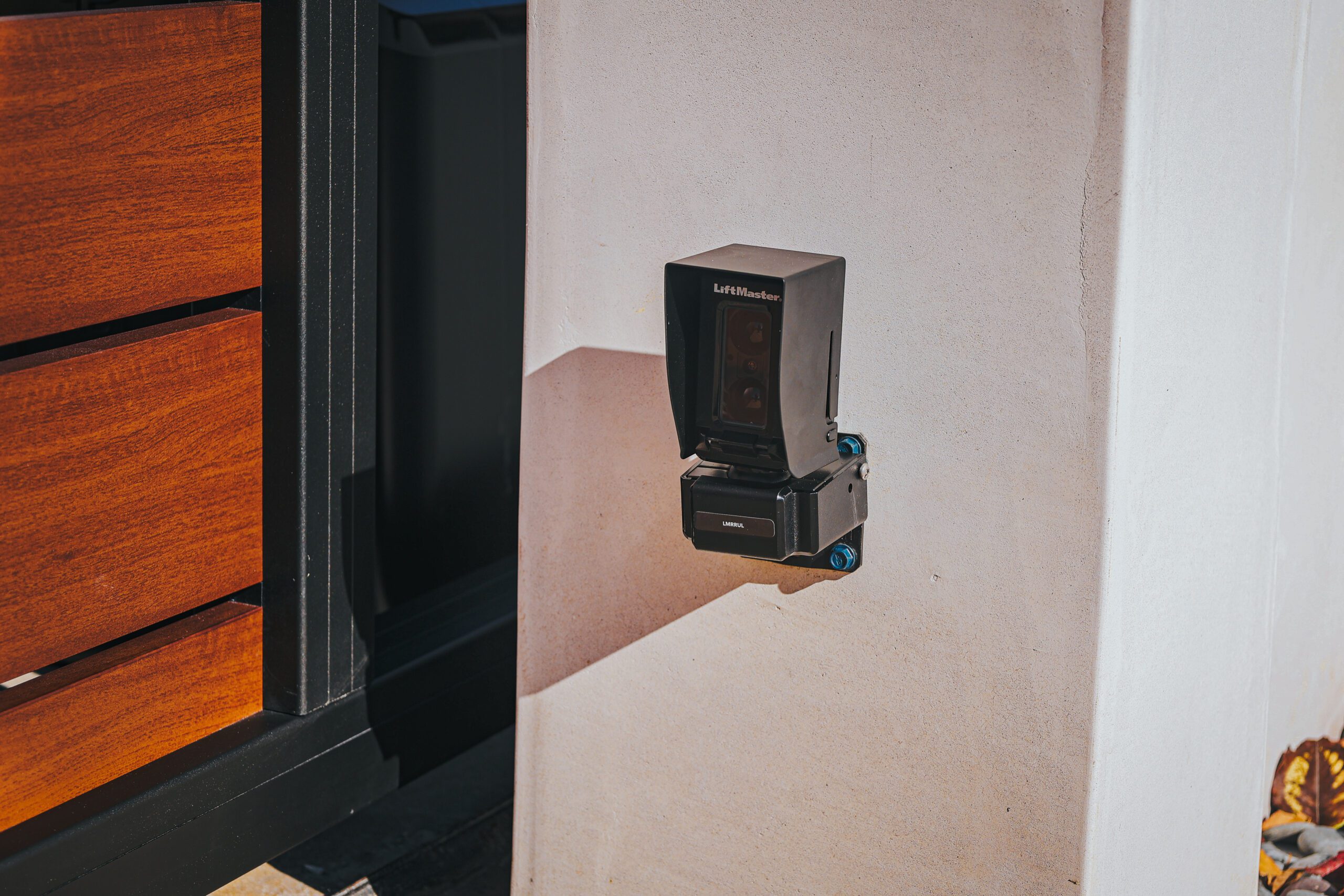 A close-up of a LiftMaster gate opener mounted on a stucco wall beside a wooden fence.