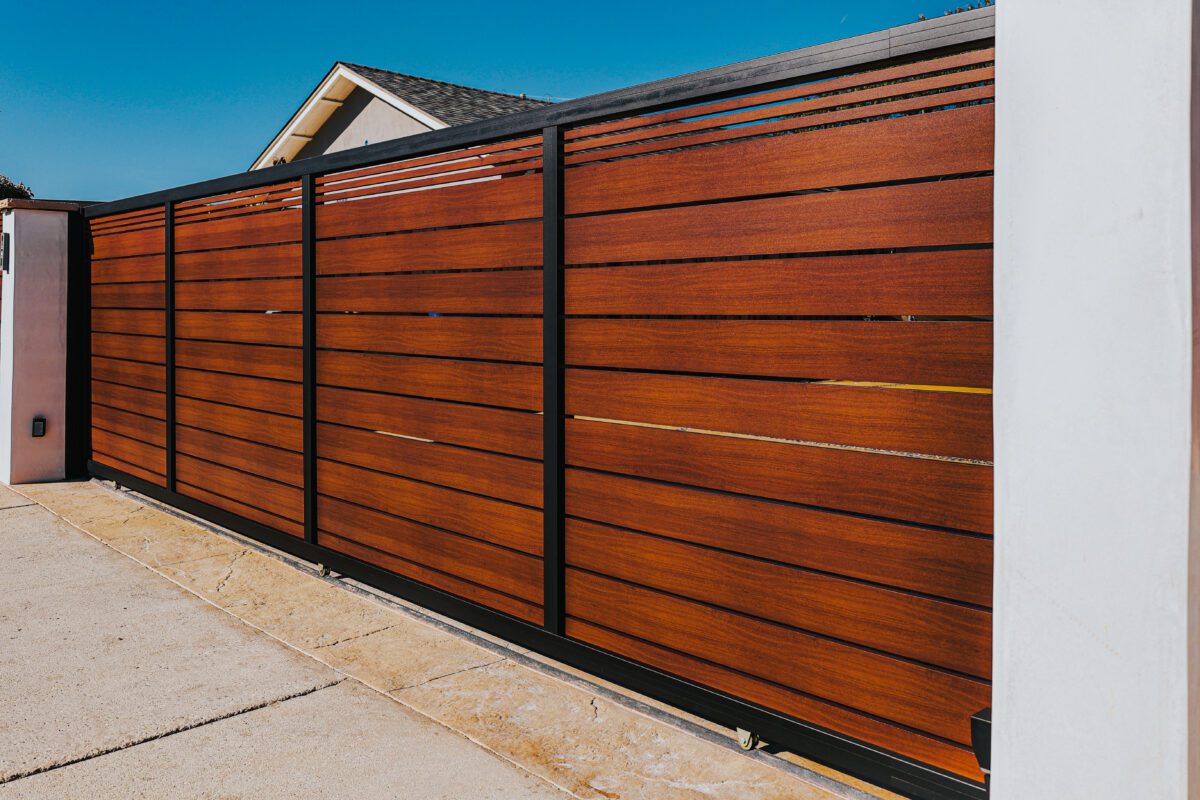Modern aluminum fence installation with a wood-like finish against a clear blue sky.