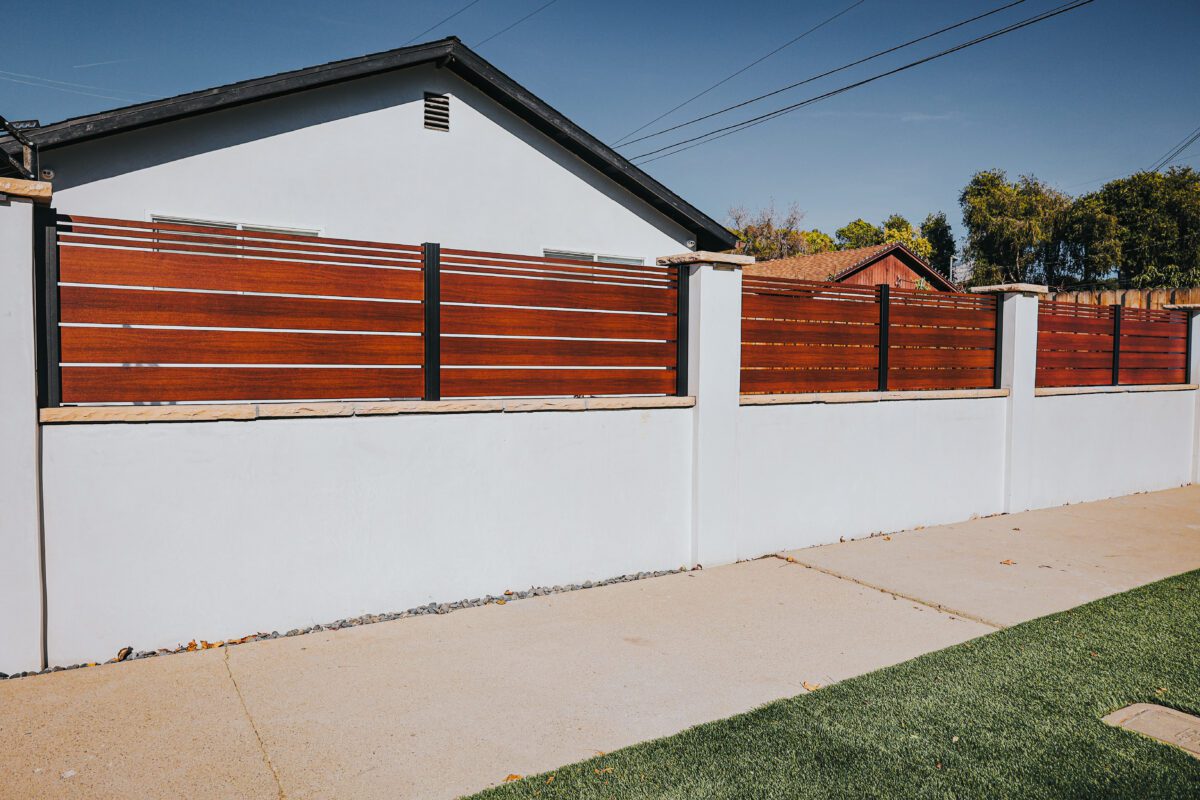 Modern aluminum fence installation with wood-like slats and white concrete base.