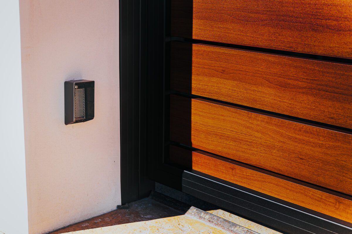 Modern aluminum gate with a wood-like finish, installed beside a stucco wall.