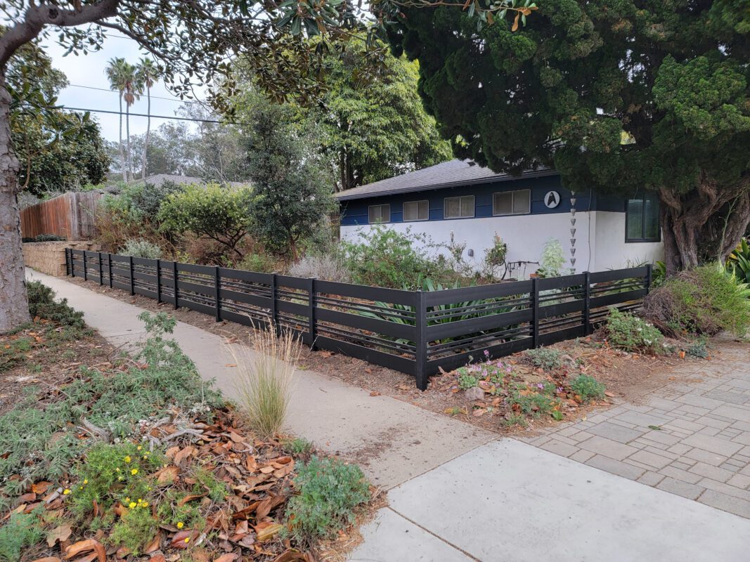 A sleek black aluminum fence lines a suburban front yard with greenery and pathways.