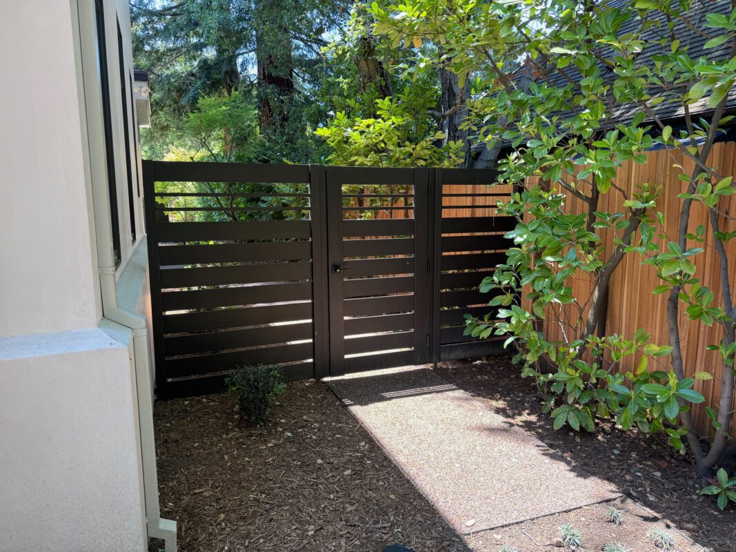 A custom bronze aluminum gate with slats, surrounded by greenery in Menlo Park.