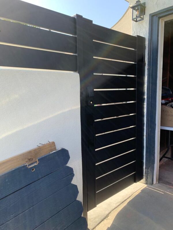 Black aluminum fence gate and wall top installation project in sunny outdoor setting.