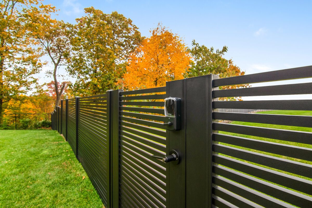 Modern black aluminum fence with a locking mechanism, surrounded by autumn foliage.