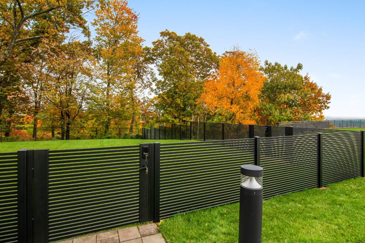 Modern black aluminum fence enhances a property surrounded by colorful autumn trees.