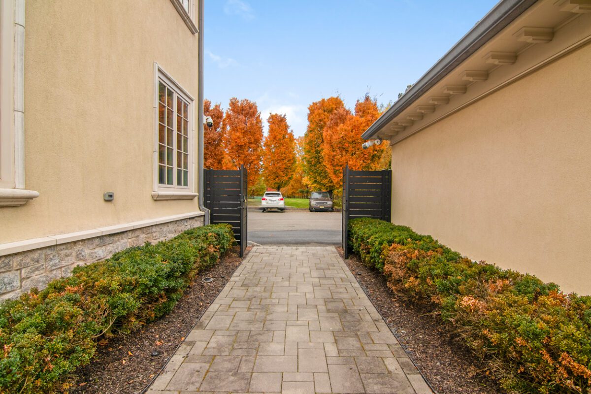 Modern black aluminum fence framing a path leading to a driveway with autumn trees.