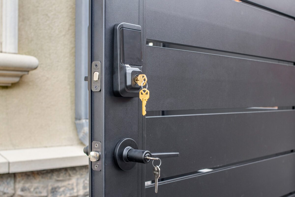 Close-up of a modern black aluminum fence gate with a lock and keys visible.