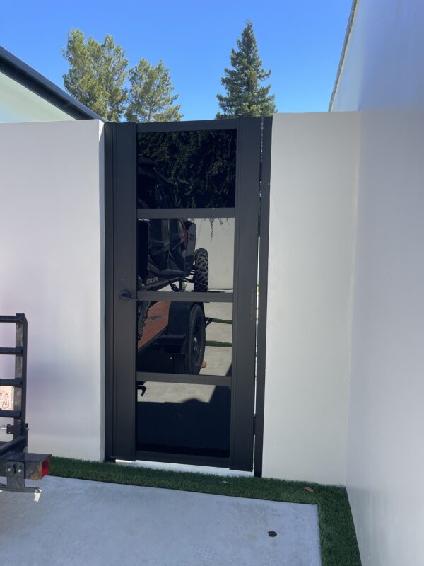 A modern black acrylic gate installed between white walls in a sunny outdoor setting.