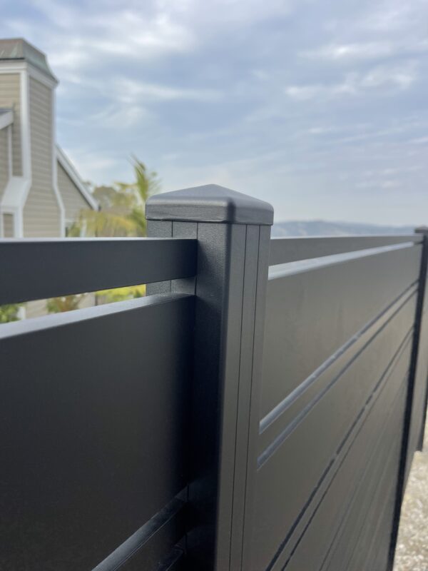 Close-up of a modern black aluminum fence post with a cloudy sky backdrop.