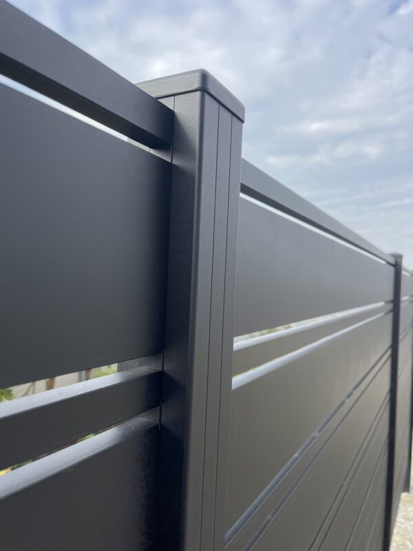 Close-up of a modern black aluminum fence installation against a cloudy sky.