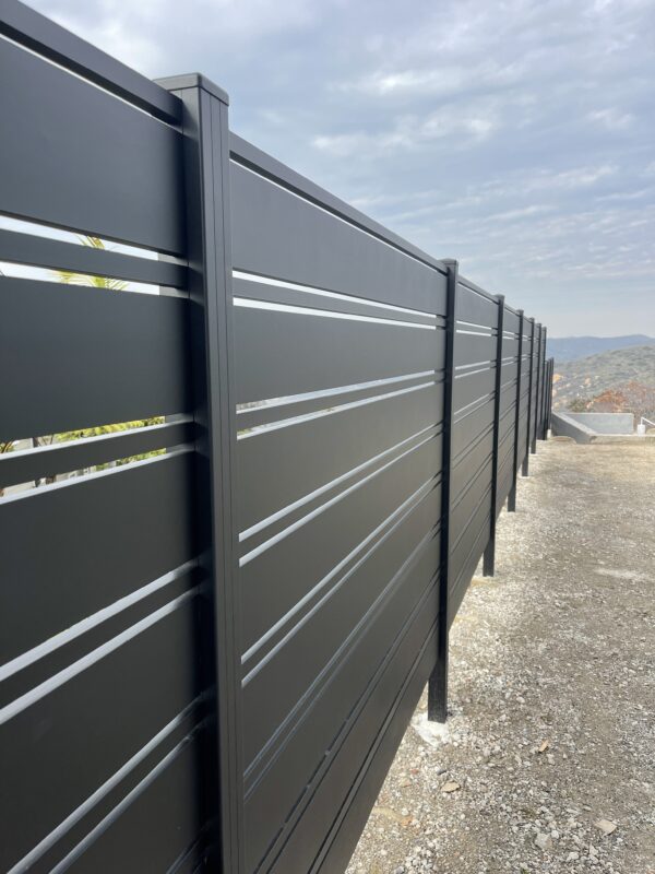 Modern black aluminum fence installation against a cloudy sky in Laguna Beach.