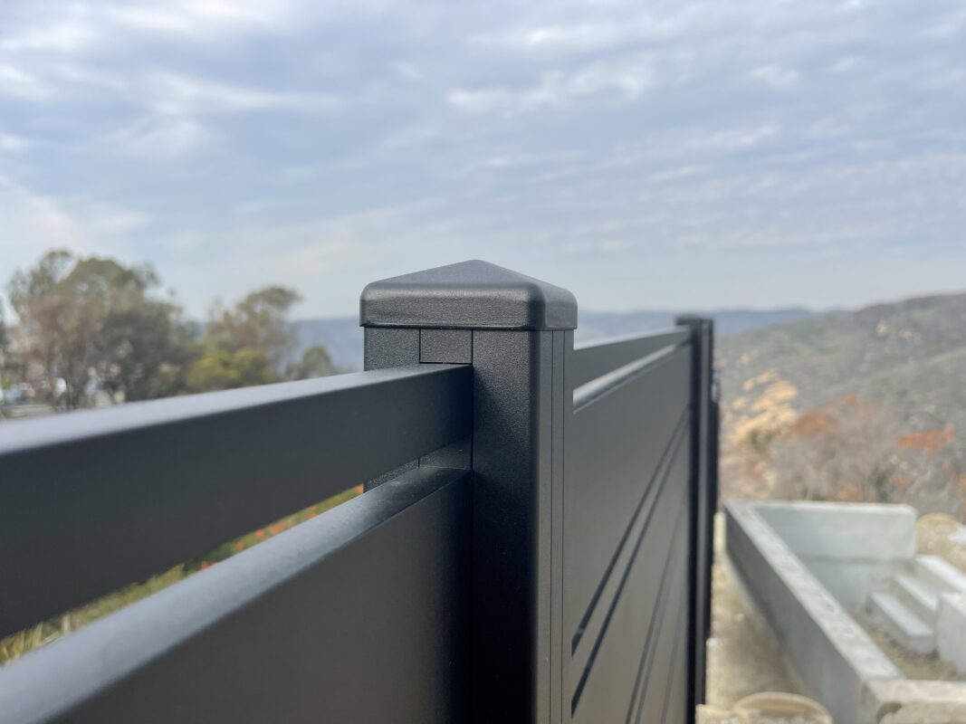 Close-up of a modern black aluminum fence post with a scenic landscape in the background.