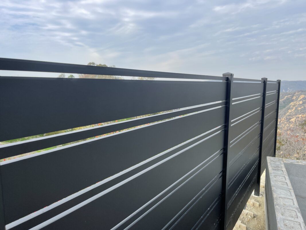 Modern black aluminum fence providing security and style in a picturesque landscape.