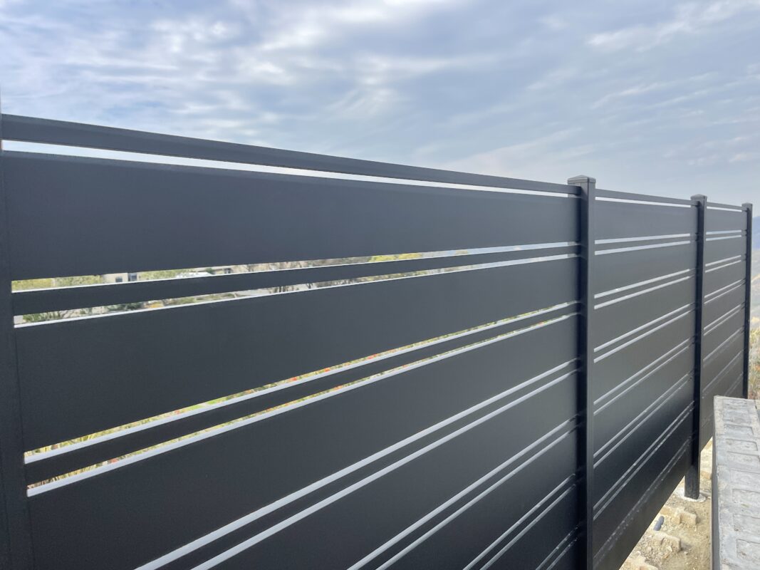 Close-up of a modern black aluminum fence under a cloudy sky in Laguna Beach.
