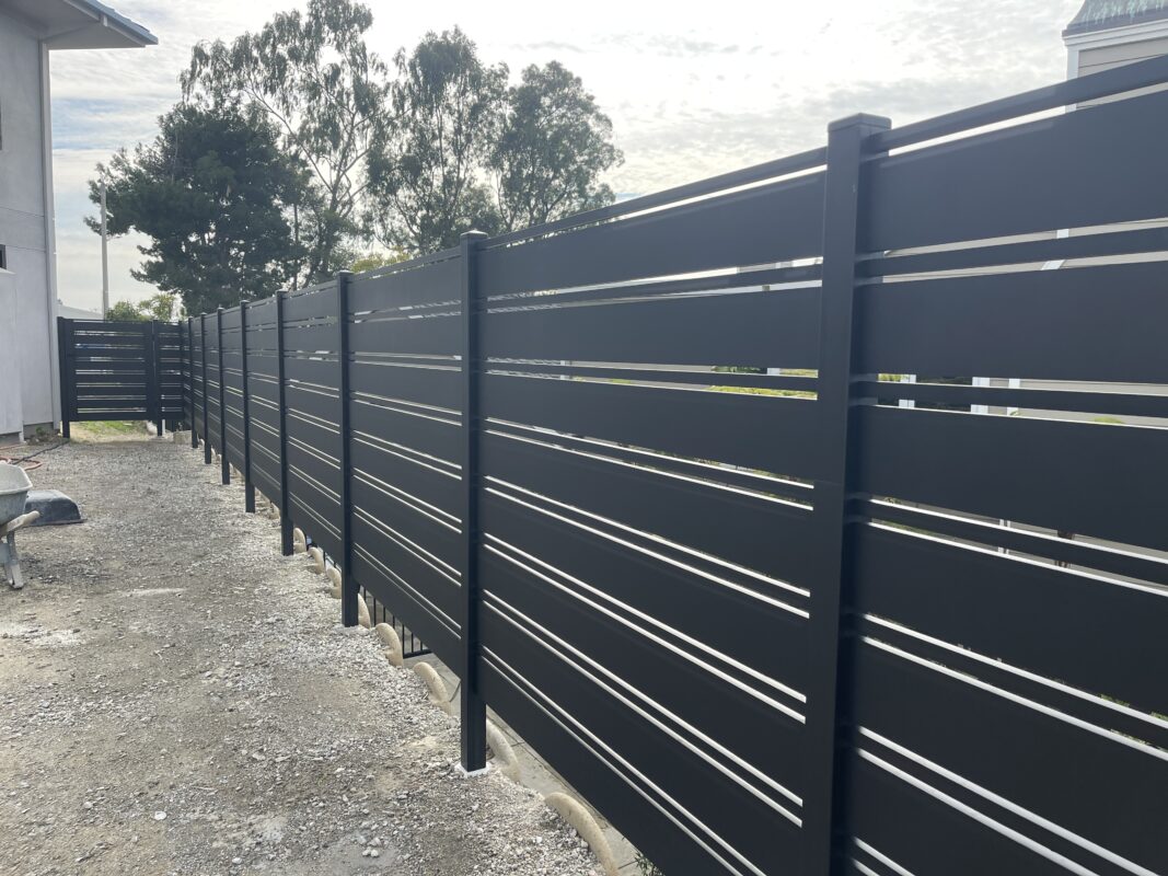 A modern black aluminum fence installation in progress along a gravel pathway.