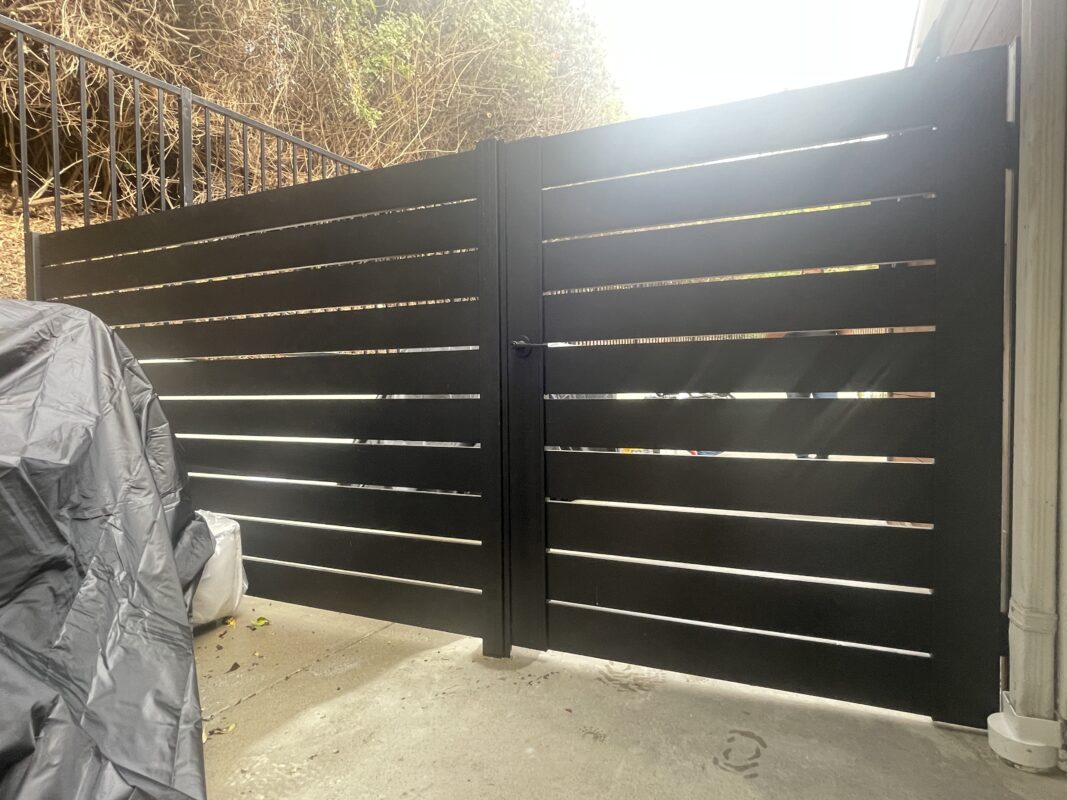 Modern black aluminum fence and gate installation in a residential setting.