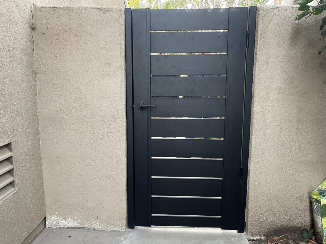Black powder-coated aluminum gate installed against a textured beige wall.
