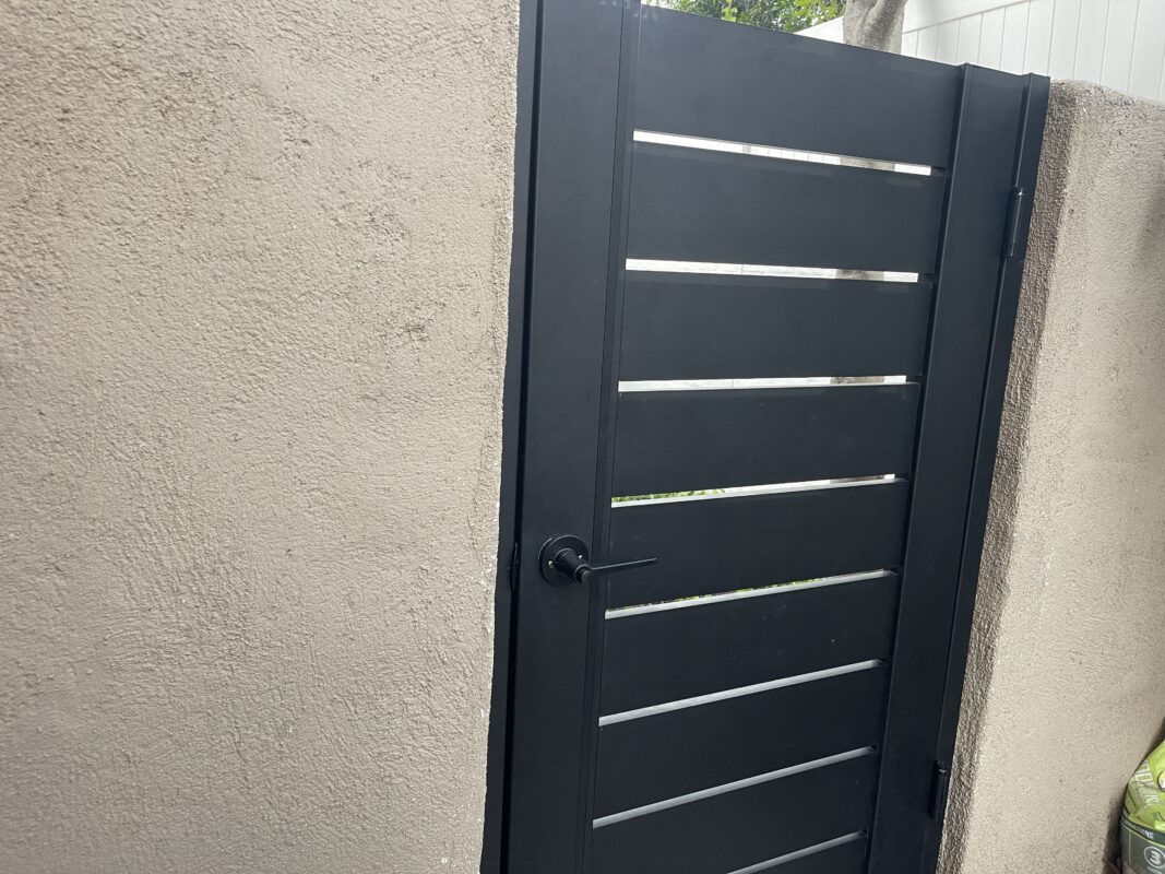 Black powder-coated aluminum gate installed next to a textured wall.