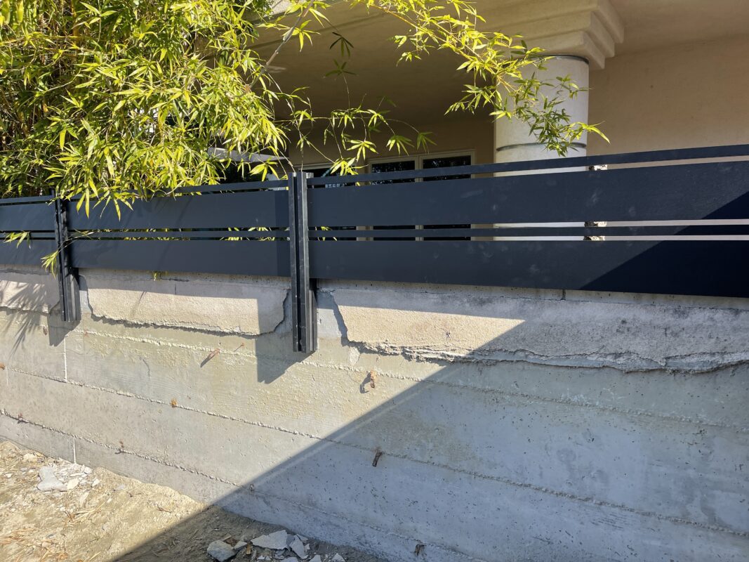 Installation of a modern black aluminum fence alongside a concrete base, surrounded by greenery.