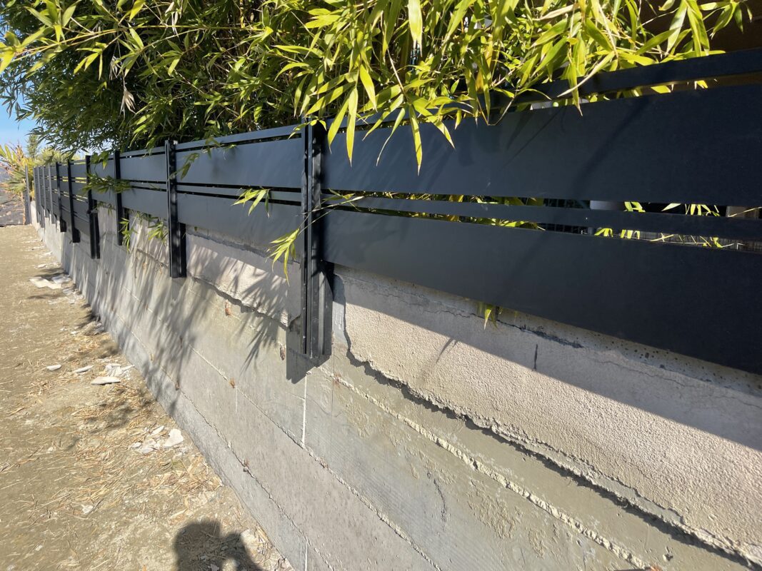 Modern black aluminum fence atop a concrete wall, surrounded by lush greenery in Laguna Beach.