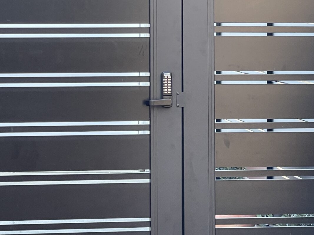 Black aluminum double swing gates with keypad lock, showcasing sleek contemporary design.