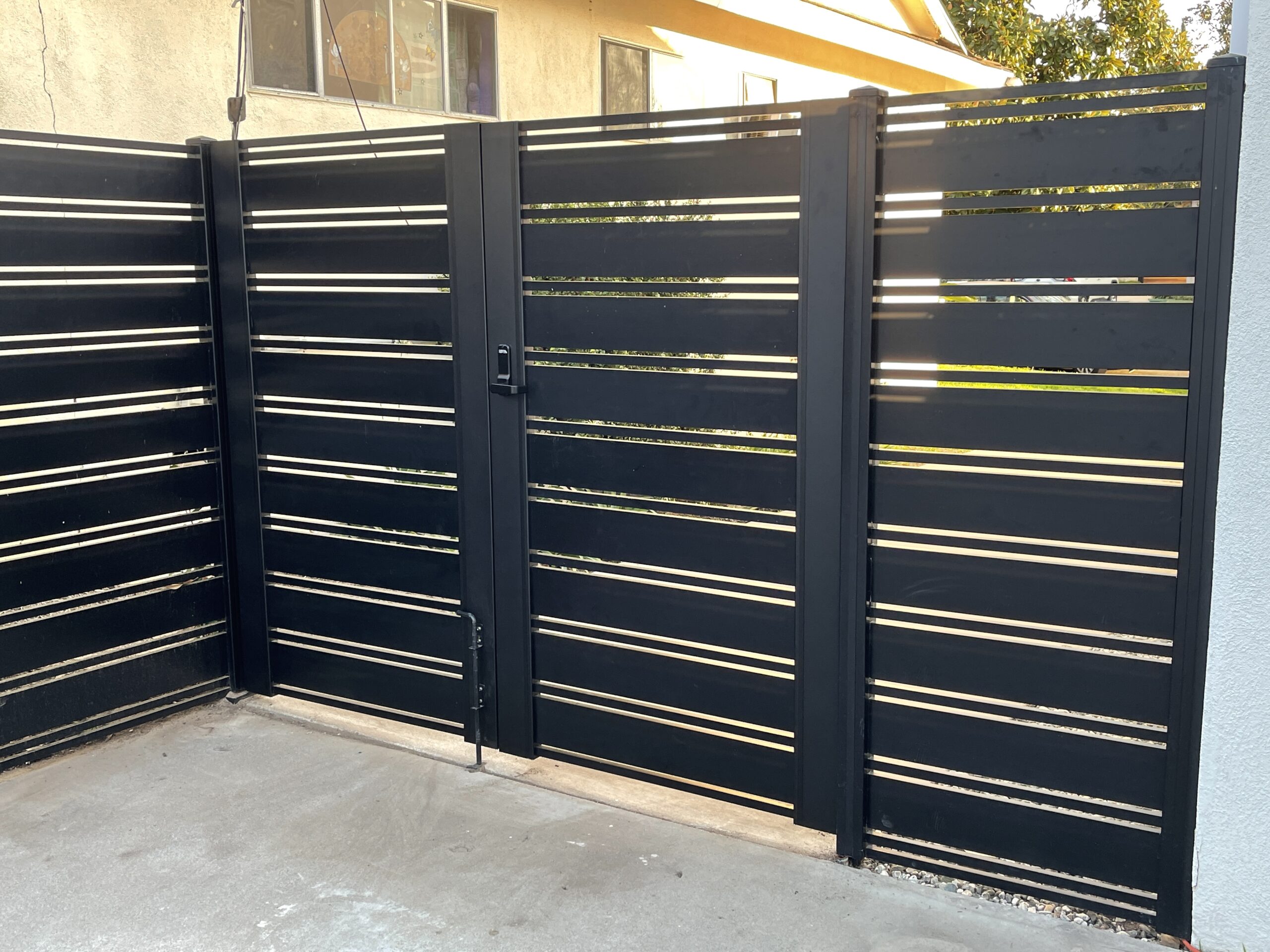 Black aluminum double swing gates with horizontal slats in a modern fence installation.