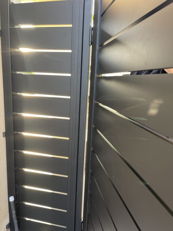 Close-up of a modern black aluminum side yard gate with horizontal slats.