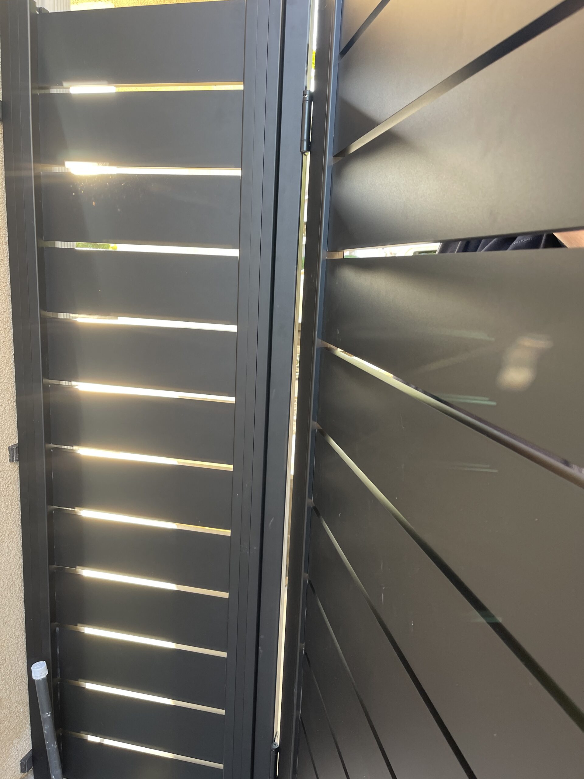 Close-up of a modern black aluminum side yard gate with horizontal slats.