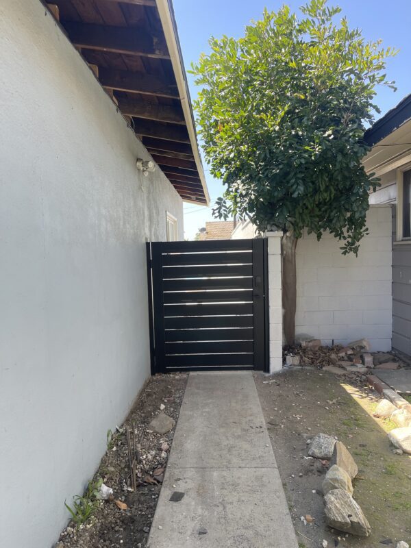 Modern black aluminum side gate beside a house, featuring a concrete pathway and greenery.