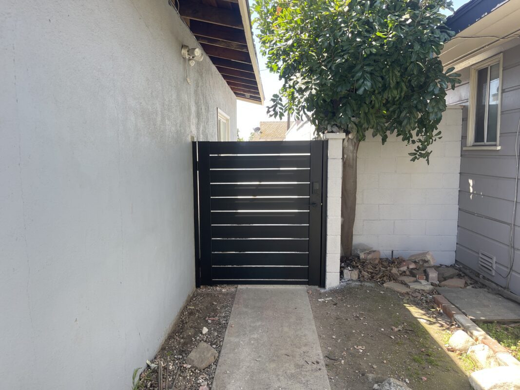 Modern black aluminum side gate in a residential setting with concrete pathway.