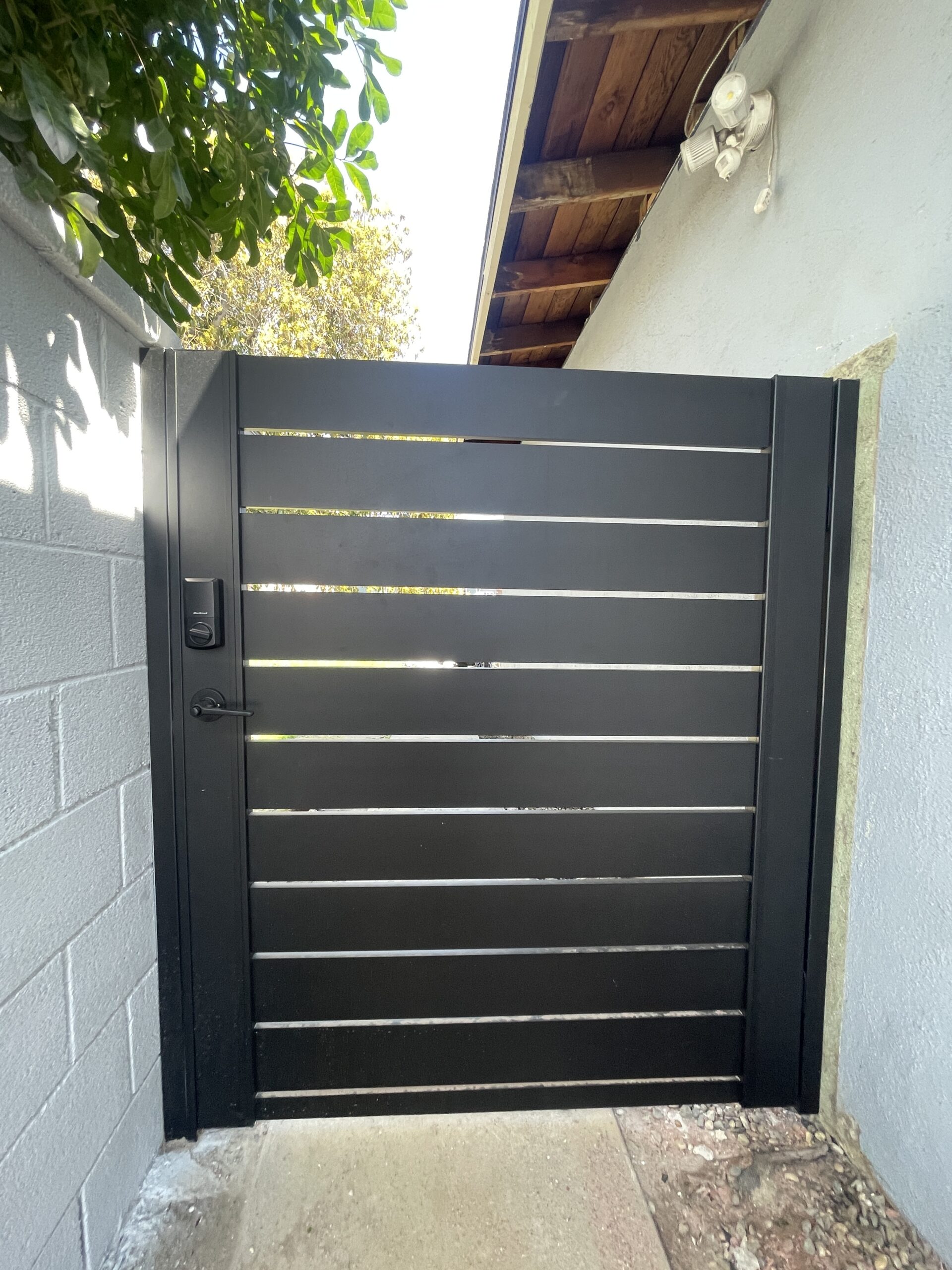 Modern black aluminum gate installed beside a house, surrounded by greenery.