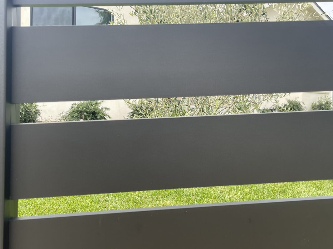 Modern black aluminum fence with greenery visible through the slats in North Hollywood.