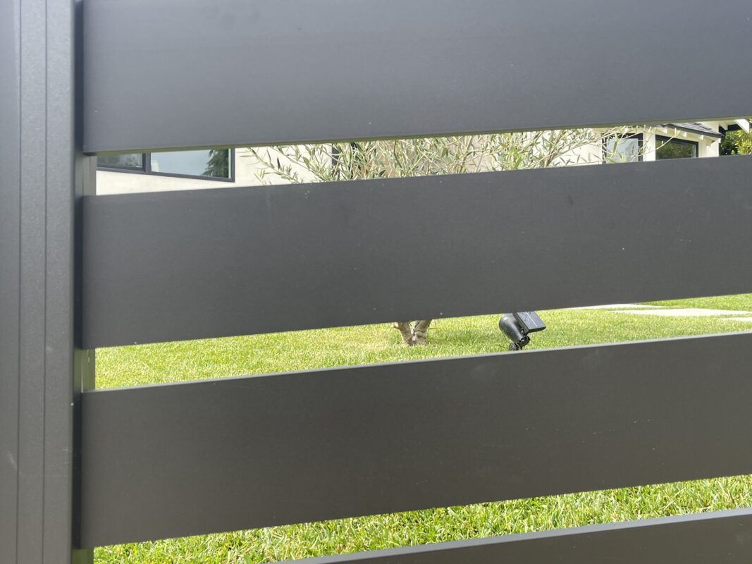 Modern black aluminum fence with a view of green grass and house in North Hollywood.