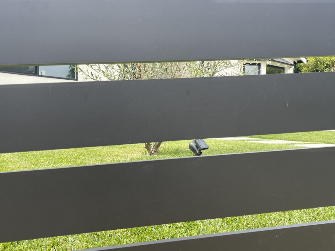 A modern black aluminum fence with horizontal slats in a front yard setting.