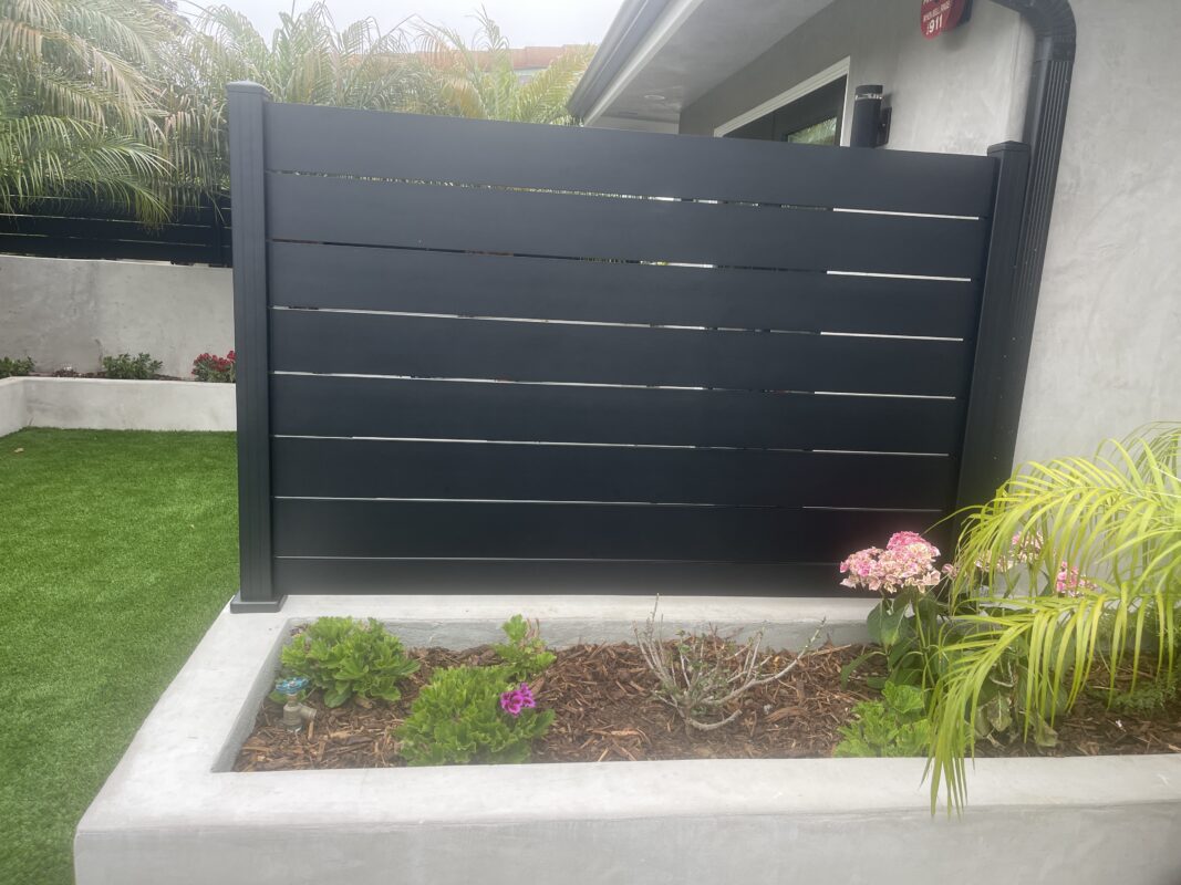 Modern black wall topper enhances privacy in a landscaped outdoor space.