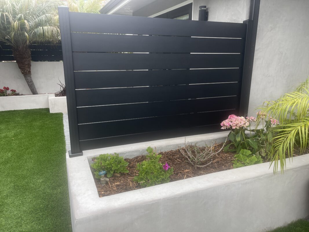 Modern black fence topper enhances landscaping with vibrant plants in a coastal setting.